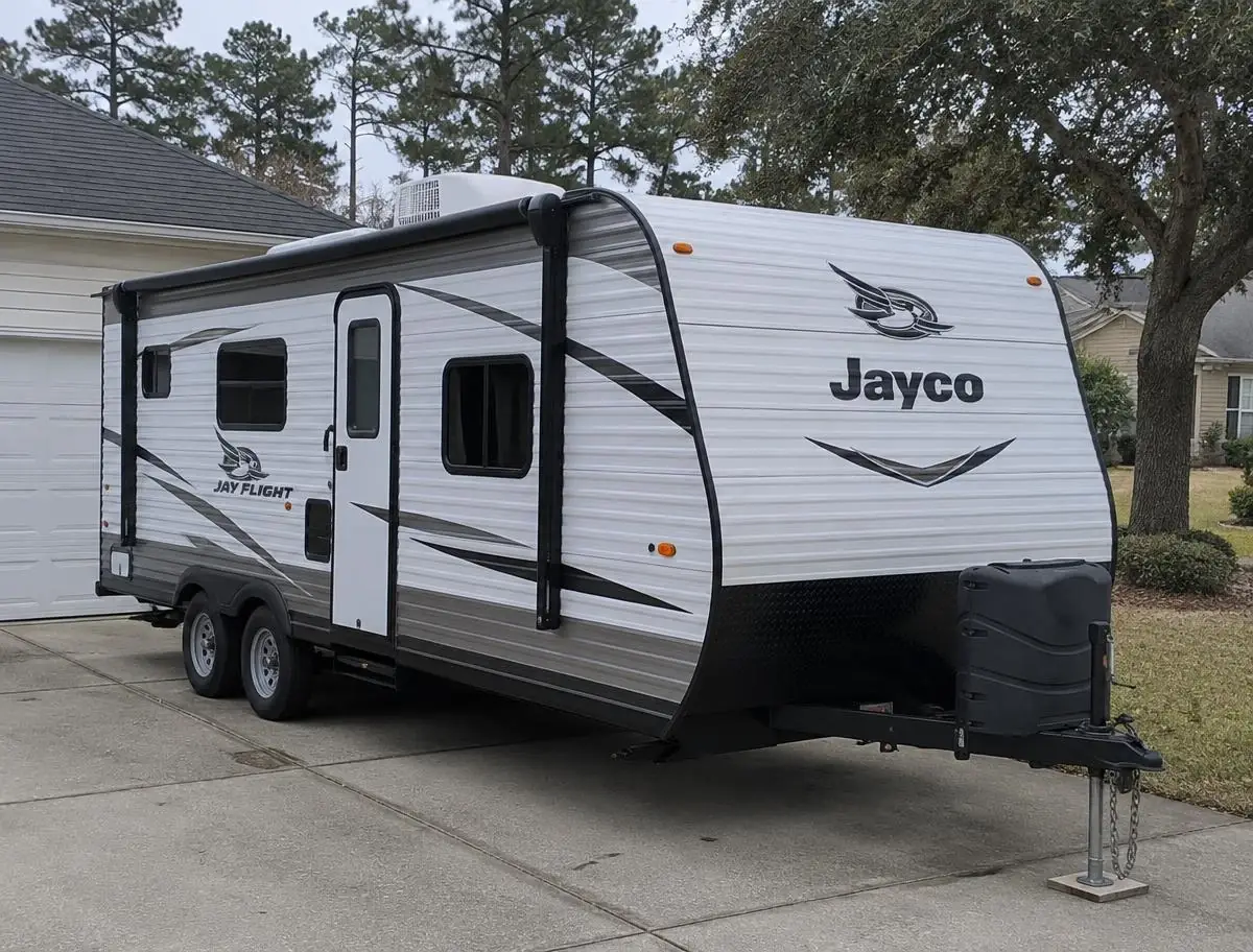 RV Air Conditioner Repair in Kempsville Travel trailer with a rooftop air conditioner parked in a residential driveway beside a garage and mature trees under an overcast sky